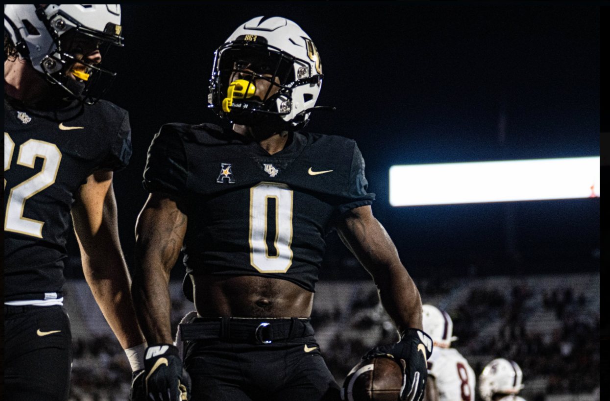 UCF running back number 0 holding the ball after a touchdown under the lights